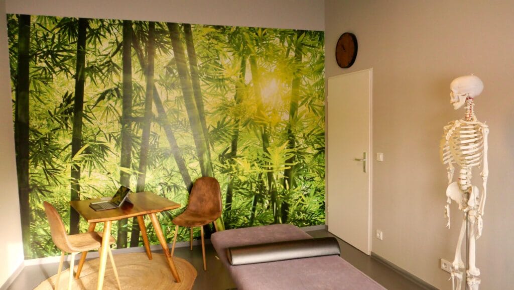 Praxisraum Behandlungsraum mit Therapieliege, Stuhl und beruhigenden Waldmotiv an der Wand in der Praxis von Sebastian Ziegler in München Bogenhausen. Nach Kontaktaufnahme und Terminvereinbarung werden Sie hier behandelt