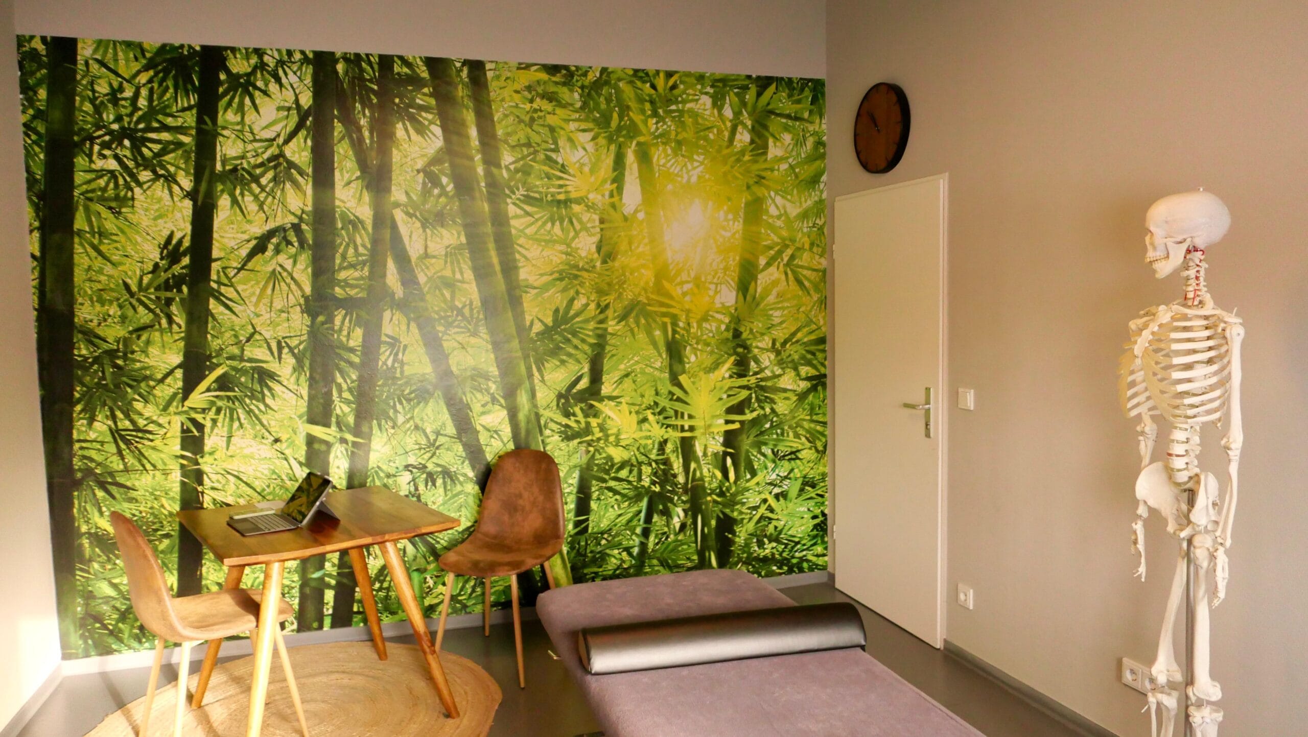 Praxisraum Behandlungsraum mit Therapieliege, Stuhl und beruhigenden Waldmotiv an der Wand